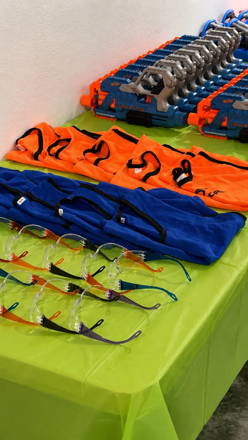 Foam blasters, team vests, and protective eyewear arranged on the safety gear table